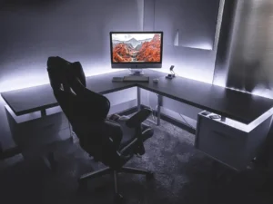 Fotel ergonomiczny gamingowy przy biurku w nowoczesnym biurze domowym, z dużym monitorem i podświetleniem LED