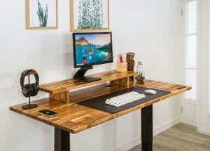 Biurko elektryczne – zdrowie i produktywność: drewniany blat z regulacją wysokości, monitor na podwyższeniu i ergonomiczne stanowisko pracy.
