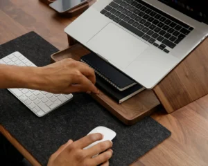 Mata na biurko – ochrona i styl: ciemnoszara filcowa mata na drewnianym blacie, laptop na podstawce, klawiatura i mysz — ergonomiczne stanowisko pracy.