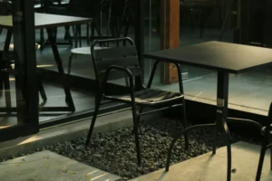 Czarne krzesło metalowe przy stoliku w ogródku kawiarnianym; industrialny, minimalistyczny design, odporne na warunki zewnętrzne.