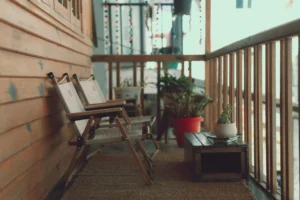 Dwa stylowe krzesła składane z drewnianą ramą i jasnym płóciennym siedziskiem, ustawione na przytulnym, drewnianym balkonie.