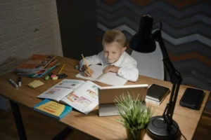 Krzesło dziecięce do biurka wspiera prawidłową postawę chłopca, który skupia się na odrabianiu lekcji.