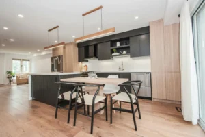 Nowoczesny stół i krzesła do kuchni z jasnego drewna i czarnymi krzesłami w stylu skandynawskim, ustawione w otwartej kuchni z czarnymi i drewnianymi szafkami.